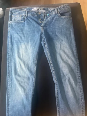 Ljusblå raka jeans med knappgylf - Säljer ett par ljusblå jeans med raka ben och klassisk femficksmodell. Jeansen har knappgylf och subtila slitningar framtill för en avslappnad look. Materialet är denim i bomull och passformen är normal. Perfekta till en casual outfit.