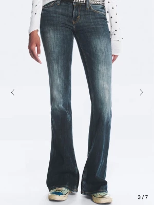 Blå bootcut jeans från Cheap Monday - Säljer ett par blå bootcut jeans från Cheap Monday med klassisk femficksmodell och coolt grönt logopatch bak. Jeansen har en snygg tvätt med slitningar och kontrastsömmar. Perfekta för dig som gillar retrovibbar och vill ha ett par jeans med lite vidare ben.