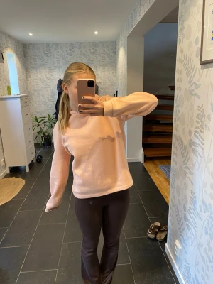 Ljusrosa hoodie med huva - Mysig ljusrosa hoodie med huva och långa ärmar. Hoodien har en enkel och clean design utan tryck eller logga, och är gjord i ett mjukt, fleeceliknande material. Perfekt för chill dagar eller när du vill ha något bekvämt och stilrent.