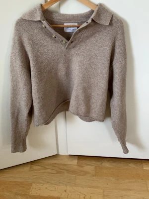Beige stickad tröja från Zara - Mysig beige stickad tröja från Zara med krage och knappdetaljer vid halsen. Tröjan har långa ärmar och ribbade muddar. Perfekt för lager på lager och enkel att matcha med olika outfits.