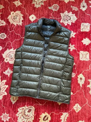 Grön dunväst med dragkedja - Snygg grön dunväst med horisontella sömmar och hög krage. Västen har dragkedja framtill och två sidofickor. Perfekt att slänga över en hoodie eller tröja för extra värme. Tillverkad i lätt och smidigt material som håller dig varm utan att kännas klumpig.