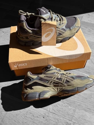 ASICS sneakers i olivgrönt och grått - Snygga ASICS sneakers i olivgrönt och grått med mesh och mockadetaljer. Skorna har en chunky sula och klassisk snörning. Perfekt för dig som gillar streetwear och vill ha en bekväm och trendig look.