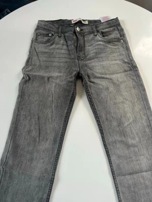 Gråa raka jeans från Levi's - Snygga gråa jeans från Levi's med klassisk femficksmodell och raka ben. Jeansen har en ljus tvätt och detaljer som Levi's ikoniska bakfickor med söm och patch i midjan. Perfekta för en avslappnad och trendig look.
