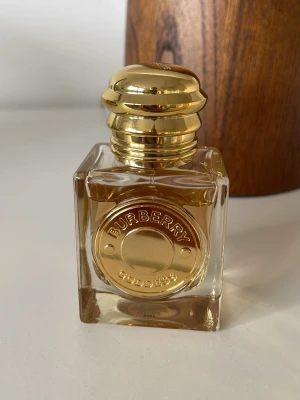 Burberry Goddess parfym 30ml - Burberry Goddess parfym i en elegant fyrkantig glasflaska med guldlock och gulddetaljer. Flaskan har en exklusiv känsla med tydlig Burberry-logga framtill. Doften är innesluten i en lyxig och stilren design som passar perfekt på sminkbordet.