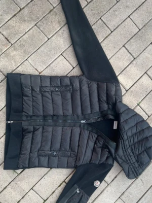 Svart cardigan moncler tricoot - Svart moncler cardigan tricoot som har 2 defekter som är tydliga där ena är ett litet hål och den andra är att ena sömen på tagen är av, Är inte helt säker på att jackan är äkta men mina vänner säger att den är men finns ingen garanti på det,    Taggar till jackan medföljer och triangel