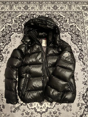 Moncler Maya - Säljer min moncler Maya pga jag har tröttnat på den. Den är i mycket fint skick på utsidan och bra kvalité. Tidningen är lite sönder och så finns de två små hål på höger arm som man ser på sista bilden, vilket gör att jag skulle kalla skicket på utsidan ”mycket bra” och på insidan ”bra” Om priset inte passar kom järna med ett nytt pris.
