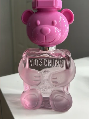 Moschino Toy 2 Bubble Gum parfym - Moschino Toy 2 Bubblegum i den ikoniska rosa nallebjörnsflaskan. En fruktig och blommig doft med toner av bubblegum, ros, citrus och saftig persika, med inslag av kryddor och trä.  100 ml och nästan helt oanvänd. Nypris 1 220 kr.
