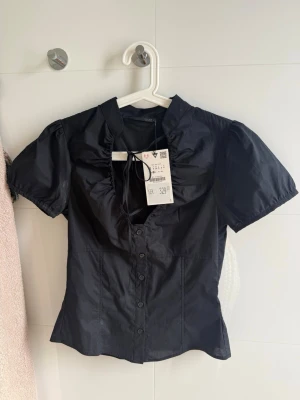 Svart blus med puffärm och knappar - Säljer den trendiga Zara toppen! Fläckarna är deo fläckar som går bort i tvätten men har ej kunnat tvätta då den har prislapp kvar! Inga defekter eller liknande är som ny! Säljs ej längre därav priset. 