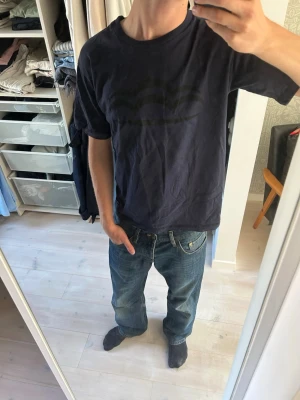 2000-tals mörkblå t-shirt med tryck - Snygg vintage mörkblå t-shirt med ett diskret svart tryck av moln på bröstet från 2000-talet! Klassisk passform med rund hals och korta ärmar. Tillverkad i mjuk bomull, perfekt för en avslappnad stil.