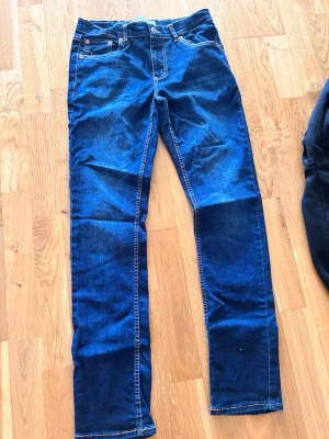 Mörkblå raka jeans - Säljer ett par mörkblå jeans med raka ben och klassisk femficksmodell. Jeansen har kontrastsömmar och är tillverkade i ett stretchigt denimtyg som ger en bekväm passform. Perfekta till vardagslooken och enkla att matcha med olika stilar.