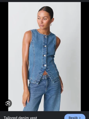 Ärmlös denimtop från Gina - Snygg ärmlös topp i blå denim från Gina med rund halsringning och knappar framtill. Toppen har figurnära passform och cool slitsdetalj nedtill. Perfekt att styla med jeans för en trendig denim-on-denim-look. Helt oanvänd💕