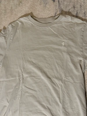 Beige t-shirt från Polo Ralph Lauren - Snygg beige t-shirt från Polo Ralph Lauren med klassisk passform och diskret broderad logga på bröstet. Tillverkad i mjuk bomull och har rund halsringning samt korta ärmar. Perfekt basplagg för en clean och stilren look.