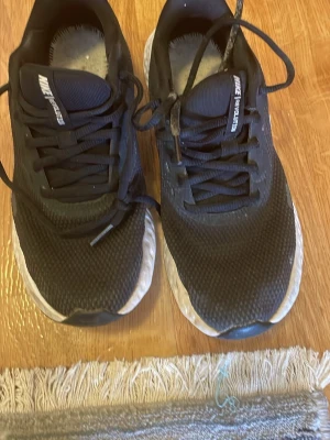 Svarta Nike sneakers med vit sula - Säljer ett par svarta Nike sneakers med vit sula och stor vit Swoosh-logga på sidan. Ovandelen är i meshmaterial för bra andningsförmåga och skon har klassisk snörning. Sulan är tjock och ger bra dämpning. Perfekta för dig som gillar sportig stil.