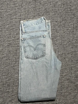 Ljusblå Levi's jeans straight fit 501 - Säljer ett par klassiska ljusblå Levi's jeans i straight fit. Jeansen har fem fickor, bälteshällor och synliga nitar. Tillverkade i 100% bomull med den ikoniska Levi's-sömmen på bakfickan. Perfekta för en avslappnad och tidlös stil.
