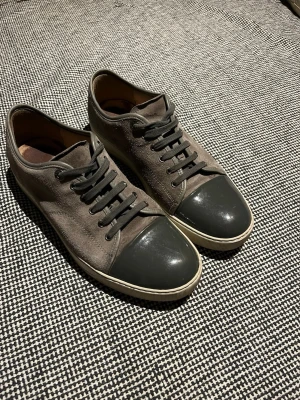 Lanvins  - Säljer ett par stilrena sneakers i grå mocka med mörkgrå tåparti i blankt material. Skorna har klassisk snörning och vit sula. Perfekta för dig som gillar en clean och enkel look.