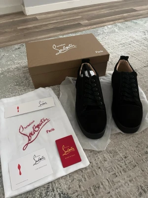 Svarta sneakers från Christian Louboutin - Stilrena svarta sneakers från Christian Louboutin i mocka med klassisk låg siluett och svarta skosnören. Insidan är ljusbeige och sulan är svart. Kommer med originalkartong, dustbag och certifikat. Perfekta för dig som vill ha en lyxig och clean look.