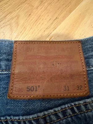 Levi's 501 blå raka jeans W31 - Klassiska blå Levi's 501 jeans med rak passform och fem fickor. Jeansen har den ikoniska läderpatchen bak i midjan och är tillverkade i slitstark denim. Perfekta för dig som gillar tidlös stil och vill ha ett par riktigt schyssta jeans.
