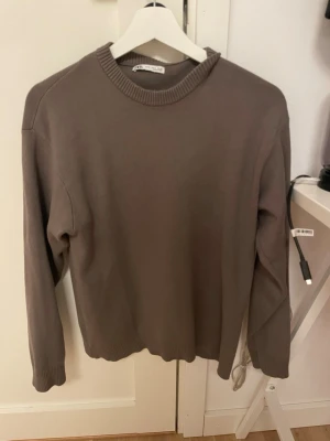 Brun tröja från Zara - En stilren brun tröja från Zara med rund halsringning och ribbade muddar. Tröjan har en enkel design och är tillverkad i ett mjukt material som passar perfekt till lager-på-lager. Perfekt för dig som gillar minimalistisk stil.