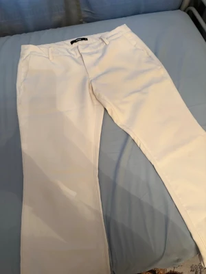 kostymbyxor Vera med slit - Snygga vita kostymbyxor från BikBok med klassisk rak passform och hällor för skärp. Byxorna har diskreta fickor och är tillverkade i ett slätt tyg som ger en stilren look. Perfekta för dig som vill ha en clean och fräsch stil.