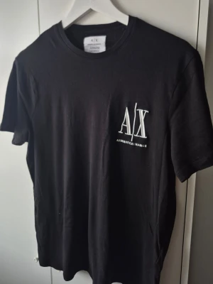 Armani Exchange t-shirt  - Säljer en svart t-shirt från Armani Exchange med vit logga på bröstet. Klassisk rund hals och korta ärmar. Tillverkad i mjuk bomull som känns skön mot huden. Perfekt för dig som gillar stilrena och tidlösa plagg.