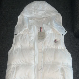 Vit dunväst från Moncler med huva - Snygg vit dunväst från Moncler med avtagbar huva och dragkedja framtill. A Kopia (Aldrig använd)