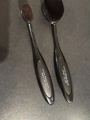 Svarta ovalformade sminkborstar Åhléns - Två svarta ovalformade sminkborstar från Åhléns, en i storlek Large och en i Small. Borstarna har täta, mjuka borst och ergonomiska handtag i plast. Perfekta för att applicera foundation, contour eller concealer med ett jämnt resultat.