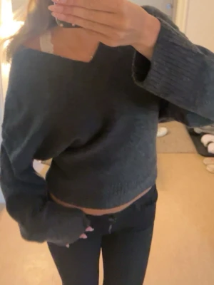 Mörkgrå off shoulder stickad tröja - Säljer en mörkgrå stickad tröja med off shoulder-modell och bred ribbstickad kant vid ärmslut och nederkant. Tröjan har en avslappnad passform och är något croppad, perfekt till höstens och vinterns outfits.