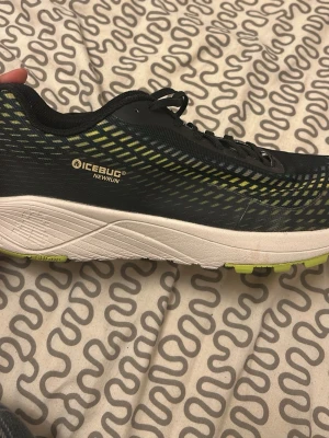Icebug NewRun löparskor med dubbar - Snygga svarta och gula Icebug NewRun löparskor med vit och limegrön sula. Skorna har dubbar i sulan för extra grepp på is och snö, perfekt för vinterlöpning. Ovandelen är i slitstark textil och syntetmaterial med coolt mönster.