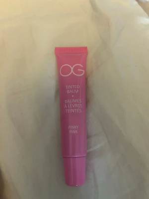 OG Tinted Balm Pinky Pink - OG Tinted Balm i färgen Pinky Pink är ett färgat läppbalsam i en smidig tub. Balsamet har en mjuk rosa nyans och kommer i en plastförpackning med skruvlock. Perfekt för dig som vill ha återfuktade läppar med en hint av färg.