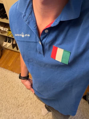 Blå Sail Racing Piké - Säljer en unik blå Sail Racing piké med italienska flaggan på bröstet och fler flaggor på ryggen. Som ny. Storlek XL, men sitter som L. Personen är 181cm och 80kg. Hör av er vid mått eller andra funderingar!😁