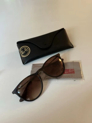 Bruna Ray-Ban solglasögon - Snygga svarta solglasögon från Ray-Ban med bruna tonade glas och klassisk båge. Kommer med originalfodral och putsduk. Perfekta för soliga dagar och ger en cool vibe till din outfit.