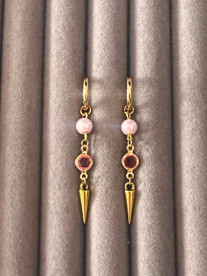 Guldörhängen med pärlor och rosa sten - Säljer ett par trendiga örhängen i guldfärgad metall med ljusrosa pärlor och rosa glittrande sten. Örhängena har en cool konformad detalj längst ner som ger en edgy touch. Perfekta för dig som vill sticka ut med snygga accessoarer.