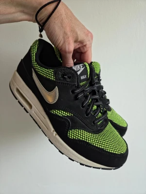 Nike Air Max 90 sneakers svart/grön - Nike Air Max sneakers med svart mockadetaljer och mesh i neonlimegrönt. Klassisk vit sula med synlig Air-enhet och silverfärgad Swoosh på sidan. Skorna har svarta skosnören och tydlig Nike Air Max-logga på plösen. Perfekta för en sportig och trendig look.