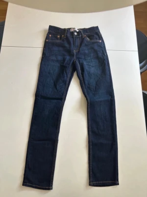Levi’s Jeans - Säljer ett par klassiska mörkblå jeans från Levi's med raka ben och fem fickor. Jeansen har kontrastsömmar och en ikonisk läderpatch bak i midjan. Perfekta till alla tillfällen och lätta att styla med olika outfits. Modellen är 512 Slim Taper. Hör av dig om du har några frågor!
