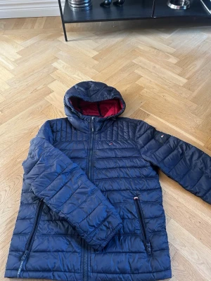 Marinblå Tommy Hilfiger jacka  - Marinblå vår jacka från Tommy Hilfiger med huva och rödfodrad insida. Jackan har quiltad design, dragkedja framtill och två sidofickor med dragkedja. Klassisk logga på ärmen och normal passform. Perfekt för kalla dagar.Finns även likande plagg i profilen. Storlek S men fungerar som M. Hör gärna av dig för frågor eller bundel deals😊😉⭐️