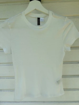 Vit t-shirt  - Klassisk vit  t-shirt från Gina Tricot med rund halsringning och korta ärmar. T-shirten har en slim passform och är tillverkad i mjuk bomull, perfekt för en enkel och clean look.
