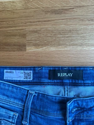 Blå jeans från Replay Anbass - Säljer ett par klassiska blå jeans från Replay, modell Anbass. Jeansen har rak passform, fem fickor och snygga söm-detaljer på bakfickorna. Tillverkade i mjukt denimtyg som sitter skönt hela dagen. Perfekta till din vardagsstil!