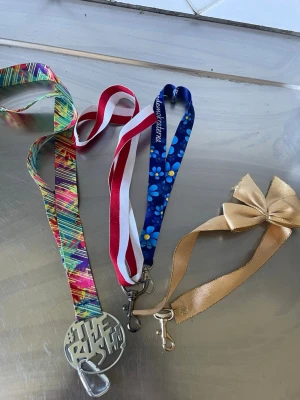 Fyra färgglada nyckelband - Säljer fyra olika nyckelband: ett med färgglatt mönster och metallbricka, ett rödvitt, ett blått med blommor och text samt ett guldigt band med stor rosett. Perfekt för att hålla koll på nycklar eller accessoarer.