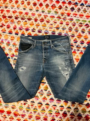 Blå slitna Jack & Jones skinny jeans - Säljer ett par blå Jack & Jones skinny jeans med slitningar och ljusa tvättade partier på låren och knäna. Jeansen har fem fickor och klassisk dragkedja med knapp. Perfekta för en avslappnad och trendig look.