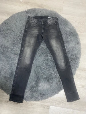 Mörkgråa Replay Jeans - Snygga svarta slim fit jeans med slitna detaljer och ljusa tvättade partier på framsidan och baksidan. Klassisk femficksmodell med dragkedja och knapp. Jeansen har vita kontrastsömmar och smal passform som sitter tajt längs benen. St 31/34 och köpta på Zalando för 1600, OBS! LÄNGD PÅ BENEN ÄR 34!