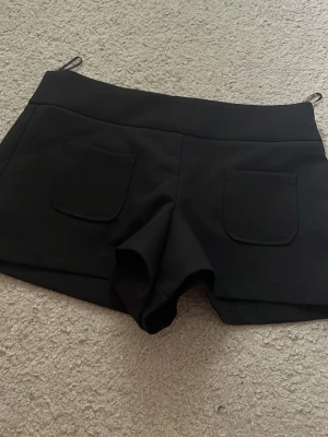 Svarta shorts med fickor från Zara  - Säljer ett par svarta shorts med två stora fickor framtill. De har en hög midja och är sydda i ett stretchigt material som ger en tight och bekväm passform. Perfekta för sommaren eller när du vill ha en enkel och stilren look.