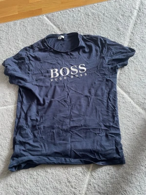 Mörkblå Hugo Boss t-shirt - Snygg mörkblå t-shirt från Hugo Boss med klassisk vit logga på bröstet. T-shirten har rund hals och korta ärmar, perfekt till jeans eller shorts. Tillverkad i mjuk bomull för skön känsla hela dagen.