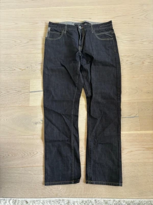 Mörkblå raka jeans med kontrastsömmar ( BUDGIVNING)  - Snygga mörkblå jeans med raka ben och tydliga kontrastsömmar. Klassisk femficksmodell med normal midja och bälteshällor. Jeansen har enkel design utan synligt märke och är tillverkade i ett robust denimtyg.