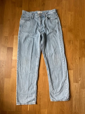 Ljusblå Jack & Jones jeans 29/32 - Säljer ett par ljusblå jeans med rak passform och hög midja. Jeansen har klassiska fem fickor, gylf med dragkedja och knapp samt ljus tvätt. Materialet är denim i bomull och de har en avslappnad vintagekänsla.