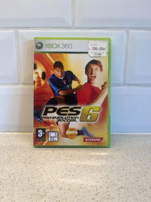 PES 6 Pro Evolution Soccer Xbox 360 - Säljer spelet PES 6 Pro Evolution Soccer till Xbox 360. Omslaget är färgstarkt med fotbollsspelare i action och spelet är i ett klassiskt grönt Xbox 360-fodral. Perfekt för dig som gillar sportspel och fotboll.
