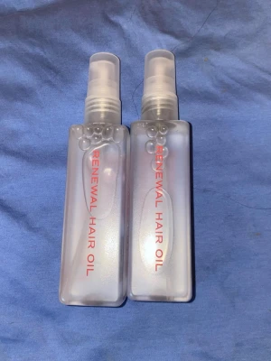 Renewal Hair Oil sprayflaskor - Två genomskinliga sprayflaskor med texten 'Renewal Hair Oil' i rött. Flaskorna är rektangulära och har vita spraymunstycken. Perfekt för dig som vill vårda och ge glans till håret med en smidig applicering. Av märket The Every nypris i gröten 450 kr styck mitt pris 399 för båda 