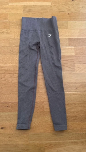 Bruna leggings från Gymshark - Snygga bruna leggings från Gymshark med hög midja. Stretchigt material som sitter skönt och följer kroppen. Diskret logga på låret och smala ben för en clean look.