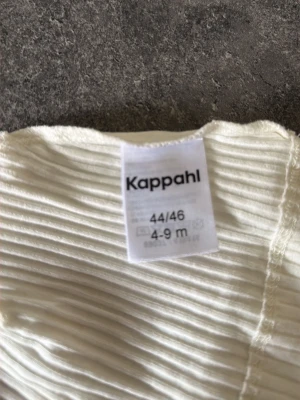 Vit ribbad mössa från Kappahl - Säljer en mjuk och stretchig vit och beige ribbad mössa från Kappahl i storlek 44/46, passar för ålder 4-9 månader. Mössan är tillverkad i ett tunt, bekvämt material och har en enkel, stilren design utan detaljer.