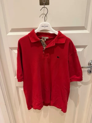 Röd piké med klassisk krage - Snygg piké från burberry i en nice röd färg. Den är stl M och i fint skick utöver ett litet pinhole som ej syns vid användning (se sista bilden). Frågor? Kom dm allt gott mvh Noah