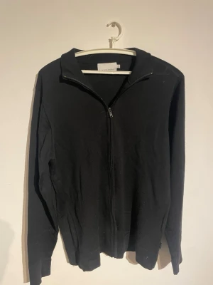 Svart zip hoodie med krage - En stilren svart hoodie med dragkedja framtill och hög krage. Hoodien har långa ärmar och är tillverkad i ett mjukt material som passar perfekt till en avslappnad look. Enkel och klassisk design utan tryck eller mönster. Nypris 100kr